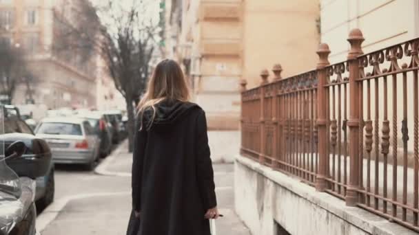 Jonge vrouw in zwarte jas lopen in het oude stadsgedeelte. Achteraanzicht van het verkennen van de stad new meisje. Slow motion. — Stockvideo