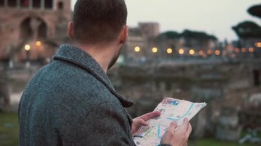 Esmer adam akşam Roma, İtalya harita Antik Roma kalıntıları çerçevede bakar. Ağır çekim.