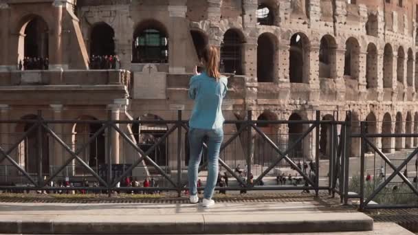Брюнетка-туристка стоит спиной к камере в Риме, Италия, фотографируя Колизей со смартфоном. Медленное движение . — стоковое видео