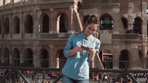 Mujer turista mira las fotos de los edificios en su teléfono inteligente. Antecedentes del Coliseo en Roma, Italia. Movimiento lento . — Vídeos de Stock