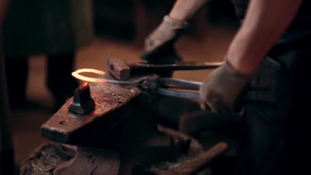 Blacksmith working with hammer and metal. Man making horseshoe on the anvil in smithy. Close-up view of workplace. — Stock Video