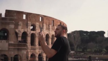 Roma, İtalya, ziyaret yakışıklı bir adam Colosseum yakınındaki fotoğraf çeker. Adam gezi, mimari sahiptir. Ağır çekim.
