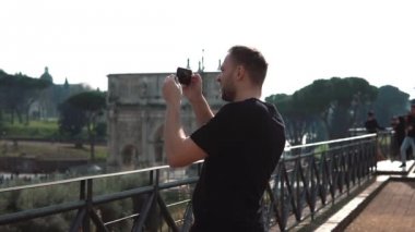 Adam turist smartphone cep telefonu ile Roma, İtalya manzara fotoğraflarını çeker. Konstantin s kemer arka plan üzerinde. Ağır çekim.