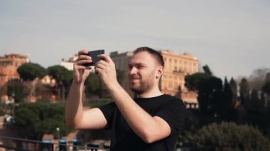 Adam turist new city araştırıyor, smartphone cep telefonu ile şehir selfie fotoğraflarını çeker. Erkek gezisi, eski binalar sahiptir. Ağır çekim.