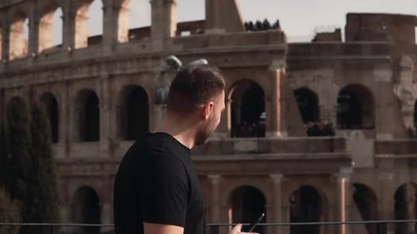 Hombre guapo con paseos en el Coliseo de Roma en Italia, tomando smartphone, explorando el país. Movimiento lento . — Vídeo de stock