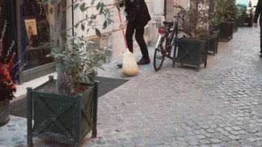 Adam hademe sokak temizler. Dükkan sahipleri hazırlar için açılış, süpürge ile çalışır. Ağır çekim.