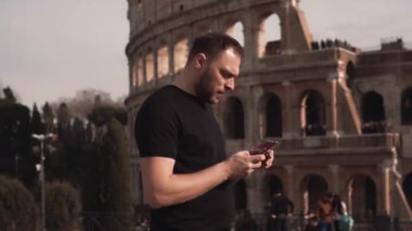 Internet hizmet veren, e-posta yazarken, fotoğrafları izlerken erkek turist Roma, İtalya. Adam Colosseum üzerinde yürür. Ağır çekim.
