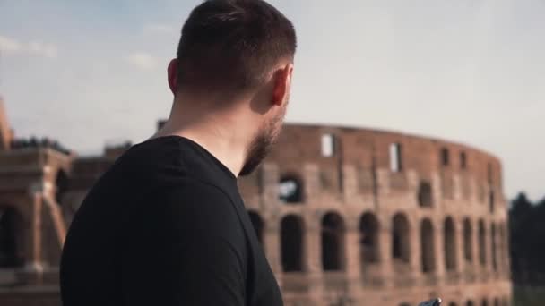 Un hombre guapo caminando por la calle en Roma, Italia, cerca del Coliseo, tomando el teléfono inteligente en sus manos. Movimiento lento . — Vídeos de Stock