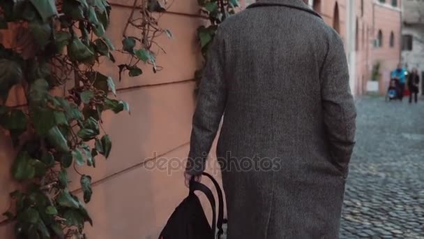 Fashionable man with backpack walking through the old street in evening. Tourist male exploring new city. Slow motion. — Stock Video