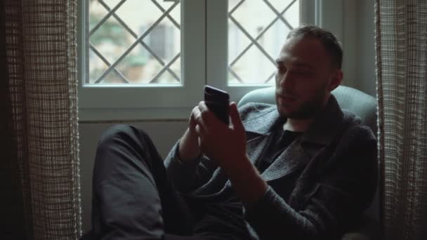 Portrait of attractive man sitting in armchair in living room and using smartphone. Stylish businessman browse Internet. — Stock Video