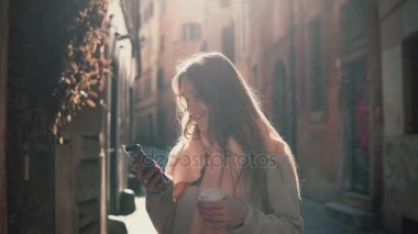 Şehirde yürüyüş ve smartphone kullanarak mutlu kadın portresi. Kız kaş belgili tanımlık enterne ve kahve içme.