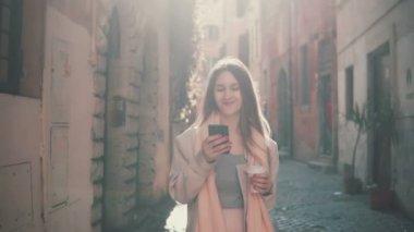 Kent merkezinde sabah saat yürüyüş, smartphone kullanarak genç mutlu bir kadın. Dalga köpüğü enterne, manifatura biriyle kız.