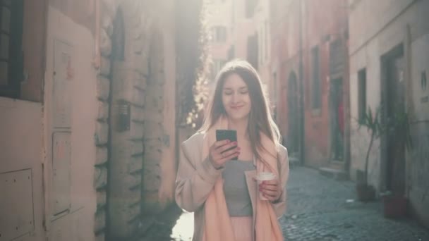 Joven mujer feliz caminando en el centro de la ciudad por la mañana, usando un teléfono inteligente. Chica navegar por Internet, mensajes de texto con alguien . — Vídeos de Stock