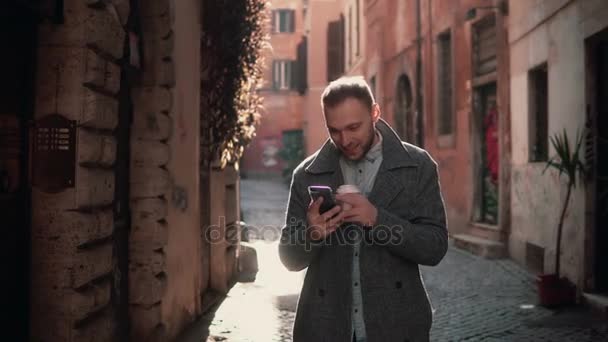 Junger attraktiver Mann, der in der Stadt spazieren geht und sein Smartphone benutzt. Mann plaudert mit Freunden und trinkt Kaffee. — Stockvideo