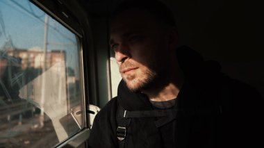 Trenle seyahat sakallı çekici bir adam. Yakışıklı genç erkek penceresine bakarak ve düşünme, gölgesinde otururken.