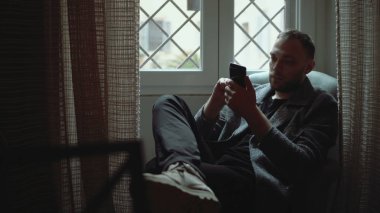 Genç yakışıklı koltuk oturma odasında otururken ve smartphone kullanarak adam. Çekici işadamı Gözat Internet.