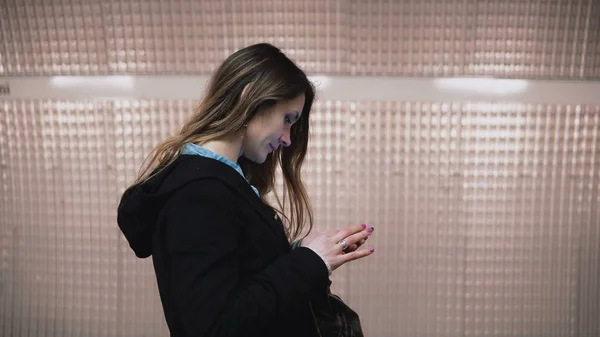 Mulher morena de pé na plataforma do metrô e usando smartphone. Menina navegando na Internet enquanto espera o trem . — Fotografia de Stock