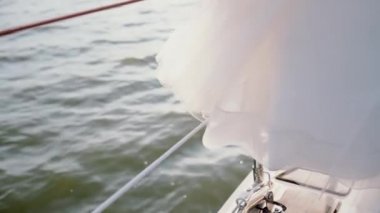 Yakın çekim sailboard kurulu bir bakış. Beyaz elbise yatta kilitleniyor. Son sürat dalgalarla gemi geçer.