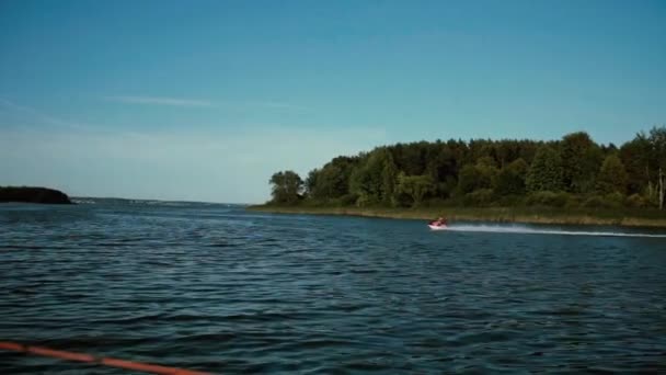 Männchen auf Wasserroller segelt mit voller Geschwindigkeit in Küstennähe mit Wald. Mann treibt Sport an sonnigem Tag. — Stockvideo