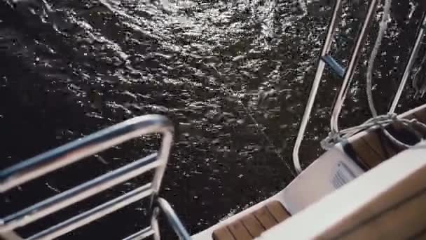 Partie arrière du voilier, la poupe traverse les vagues dans le lac. Voile dans le vent par temps ensoleillé. Vue rapprochée . — Video