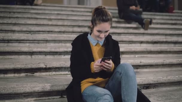 Mujer atractiva joven sentada en la escalera de la ciudad y el uso de teléfono inteligente. Estudiante chica mensajes de texto con amigos . — Vídeos de Stock