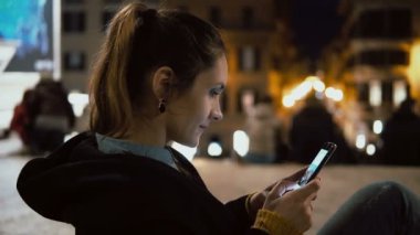 Şehir merkezinde akşam ve fotoğraf smartphone dokunmatik ekran teknolojisi ile arıyor oturan çekici esmer kadın.