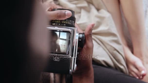 Vista de cerca del hombre africano sosteniendo la vieja cámara fotográfica, tomando la foto de la mujer cerca de la ventana. Pareja multirracial en la cama . — Vídeo de stock