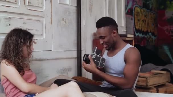 Multiracial par i pyjamas på sängen i morgon. Ung man ta bilder på den gamla photocamera, kvinna poserar. — Stockvideo