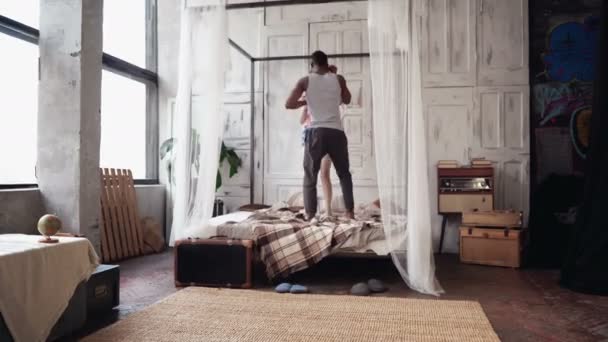 Jonge multi-etnisch paar in pyjama dansen, springen op het bed. Afrikaanse jongen en europen vrouw plezier hebben in de ochtend. — Stockvideo