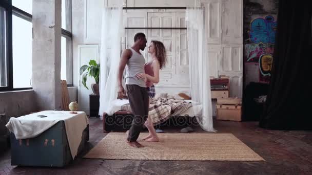 Többnemzetiségű pár pizsamában, együtt szórakoztunk. Afrikai férfi és európai nő, tánc, ugrás az ágyon, nevetve. — Stock videók