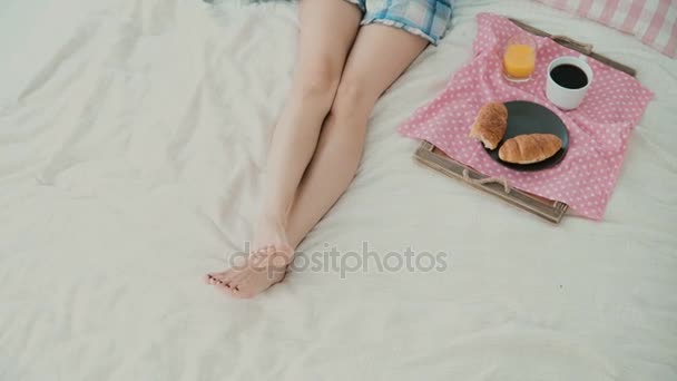 Mujer joven usando tecnología inalámbrica acostada en la cama y charlando en casa. Tipos de chica en el teléfono inteligente durante el desayuno . — Vídeos de Stock