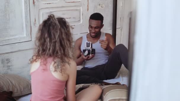 Молодий фотограф фотографує рухому кінокамеру кучерявої жінки в піжамі. Пара в веселому гуморі . — стокове відео