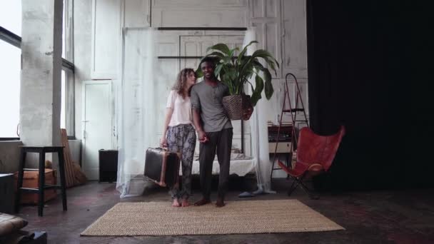 Multiethnic couple gather in travel. Woman holds suitcase, man holds plant. Boy and girl kisses and goes away. — Stock Video