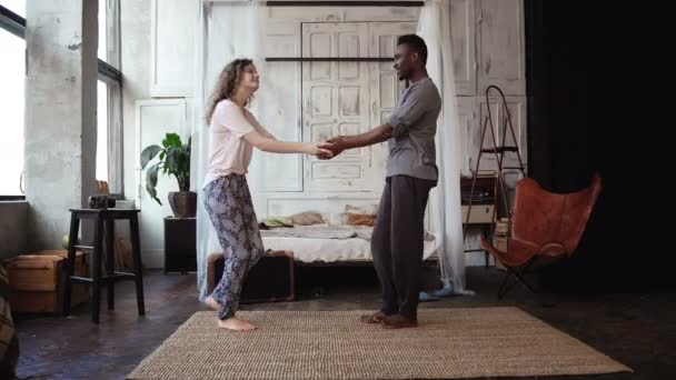 Pareja multiétnica bailando en pijama. Africano macho y caucásico hembra mirada feliz, riendo y sonriendo, tomados de la mano — Vídeos de Stock