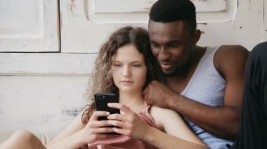 Çok ırklı çift belgili tanımlık smartphone kullanın. Erkek ve kadın pijama dokunmatik ekran teknolojisi ile Internet sörf.