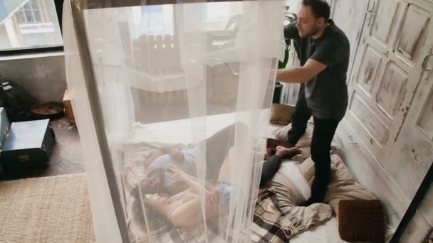 Многонациональная пара на фотосессии. Фотограф записывает видео во время лежания мужчины и женщины на кровати, использует смартфон . — стоковое видео
