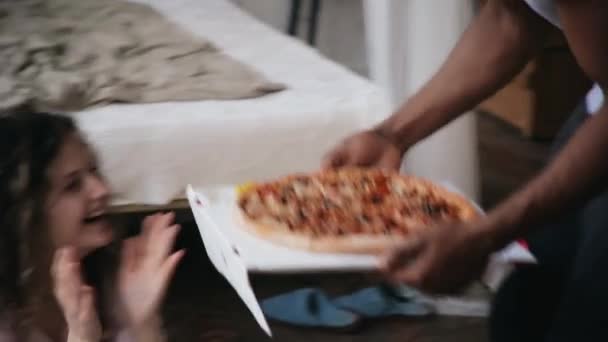 Hombre africano en pijama trae pizza a mujer caucásica hambrienta. Pareja multiracial en pijama huele la comida rápida . — Vídeos de Stock