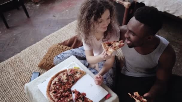 Kvinna erbjuder pizza för att mannen, men äta skiva själv. Multiracial par ha kul under måltiden med snabbmat. — Stockvideo