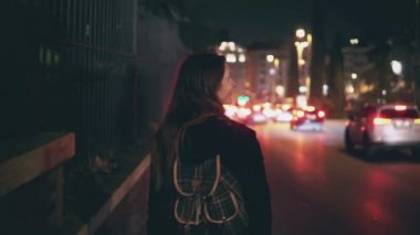Arkadan görünüşü yolun trafik zaman yürüyen esmer kadın. Kız şehrin içinden geç saatte tek başına gider..