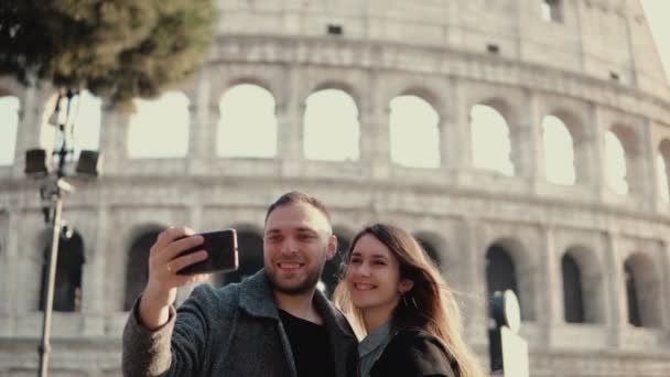 Fiatal, boldog pár utazás, Róma, Olaszország. Férfi és nő vesz a selfie fénykép smartphone közel a Colosseum. — Stock videók