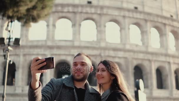 Young attractive woman and man standing near the Colosseum in Rome, Italy. Couple takes the selfie photo on smartphone. — Stock Video