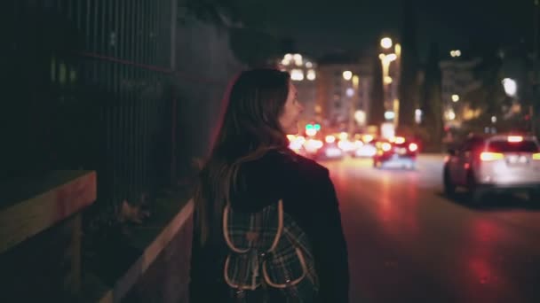 Vista trasera de la mujer morena caminando cerca de la carretera en el momento del tráfico. Chica pasa por la ciudad tarde por la noche solo . — Vídeo de stock