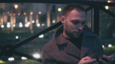 Akşam şehir ve kullanım smartphone içinde oturan çekici genç adam portresi. Yakışıklı erkek Gözat Internet.