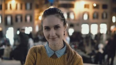 Şehir merkezinde akşam duran genç güzel kadın portresi. Öğrenci kız görünüyor kameraya, gülümseyen.