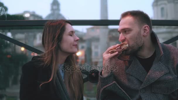 젊은 매력적인 부부 도심에서 휴식을 있다. 남자와 여자 저녁 야외에 앉아 샌드위치를 먹는. — 비디오