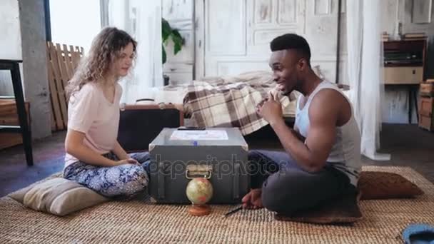 Multiracial par i pyjamas sitter på golvet och spelar vildsvin. Kvinnan kastar tärningarna, man väntar sin tur. — Stockvideo