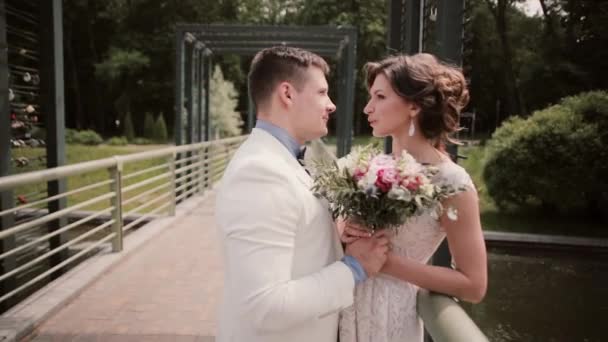 Seitenansicht eines wunderschönen Liebespaares am Hochzeitstag. Braut im weißen Hochzeitskleid, Bräutigam im Kleid auf einer Brücke — Stockvideo