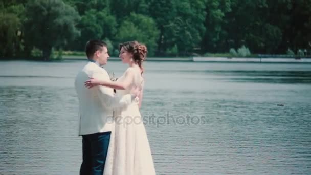 Wedding day. Beautiful couple enjoy their happiness standing on a quay, hugging and kissing. Wedding outfit, bouquet — Stock Video