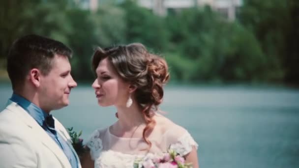 Día de la boda. Hermosa pareja disfrutar de su felicidad de pie en un muelle, besos. Traje de boda, ramo — Vídeo de stock