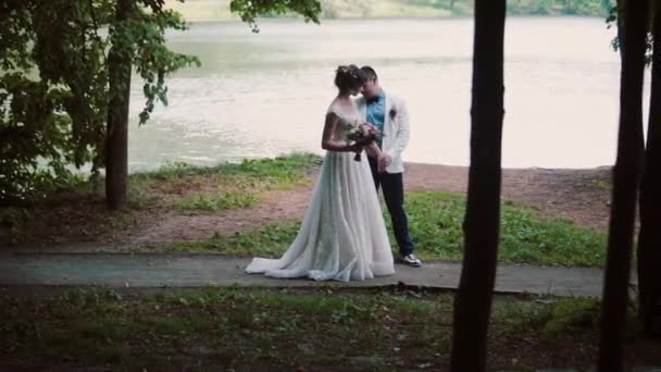 Pareja enamorada en una orilla del río el día de su boda. Feliz novia se gira y muestra su hermoso vestido a su novio — Vídeos de Stock